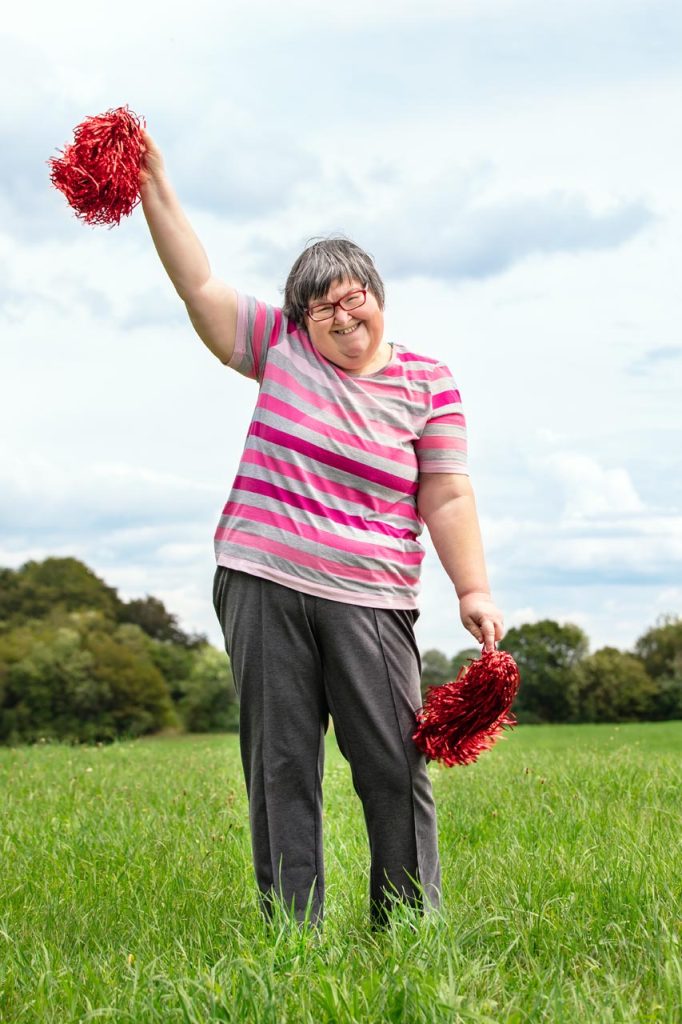 mental disabled woman is cheering with red pompons on a green meadow, having a lot of fun
